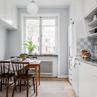Foto på ett 60 tals grå linjärt kök och matrum, med en integrerad diskho, släta luckor, vita skåp, bänkskiva i rostfritt stål, flerfärgad stänkskydd, vita vitvaror, ljust trägolv och beiget golv
