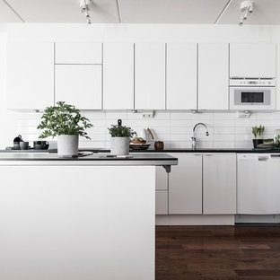 Inredning av ett skandinaviskt mellanstort kök, med släta luckor, vita skåp, vita vitvaror, en köksö, vitt stänkskydd och mörkt trägolv