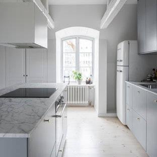 Skandinavisk inredning av ett vit vitt parallellkök, med en undermonterad diskho, släta luckor, grå skåp, vita vitvaror, ljust trägolv, en köksö och beiget golv