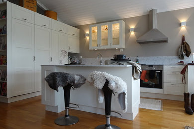 Mittelgroße Klassische Wohnküche in L-Form mit Unterbauwaschbecken, weißen Schränken, Quarzwerkstein-Arbeitsplatte, Küchenrückwand in Weiß, Elektrogeräten mit Frontblende, braunem Holzboden, Kücheninsel und weißer Arbeitsplatte in Stockholm