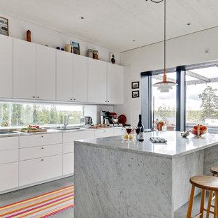 Foto på ett nordiskt parallellkök, med en integrerad diskho, släta luckor, vita skåp, marmorbänkskiva, fönster som stänkskydd, integrerade vitvaror, betonggolv, en köksö och grått golv