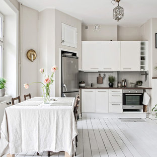 Inspiration för stora minimalistiska linjära brunt kök och matrum, med släta luckor, vita skåp, träbänkskiva, grått stänkskydd, målat trägolv, vitt golv och rostfria vitvaror