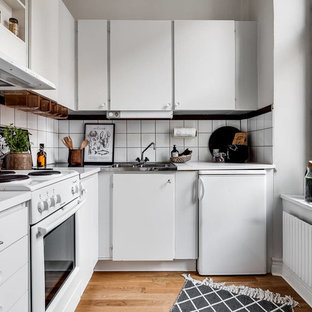 Idéer för att renovera ett avskilt, litet nordiskt l-kök, med en nedsänkt diskho, släta luckor, vita skåp, vitt stänkskydd, vita vitvaror, mellanmörkt trägolv och brunt golv
