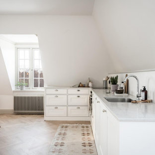 Minimalistisk inredning av ett grå grått kök, med en undermonterad diskho, luckor med infälld panel, vita skåp, mellanmörkt trägolv och brunt golv