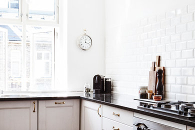 Diseño de cocinas en L nórdica con armarios con paneles empotrados, puertas de armario blancas, salpicadero blanco, electrodomésticos de acero inoxidable, suelo de madera oscura y salpicadero de azulejos de cerámica
