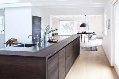 Große Moderne Wohnküche mit integriertem Waschbecken, flächenbündigen Schrankfronten, dunklen Holzschränken, Arbeitsplatte aus Holz, hellem Holzboden und Kücheninsel in Kopenhagen