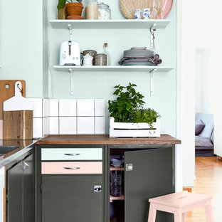 Foto på ett minimalistiskt l-kök, med en nedsänkt diskho, släta luckor, grå skåp, träbänkskiva, vitt stänkskydd och ljust trägolv