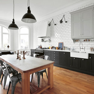 Photo of a large industrial single-wall eat-in kitchen in Copenhagen with an undermount sink, recessed-panel cabinets, black cabinets, recycled glass benchtops, black appliances, medium hardwood floors and no island.