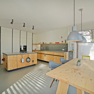 Große, Einzeilige Industrial Wohnküche mit flächenbündigen Schrankfronten, hellbraunen Holzschränken, Mineralwerkstoff-Arbeitsplatte, Küchenrückwand in Grau, Küchengeräten aus Edelstahl, Betonboden, Kücheninsel, integriertem Waschbecken und Glasrückwand in München