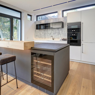 Offene, Zweizeilige, Mittelgroße Moderne Küche mit flächenbündigen Schrankfronten, weißen Schränken, schwarzen Elektrogeräten, hellem Holzboden, beigem Boden, Einbauwaschbecken und Halbinsel in München