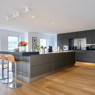 Offene, Einzeilige, Geräumige Moderne Küche mit flächenbündigen Schrankfronten, dunklen Holzschränken, Küchenrückwand in Metallic, schwarzen Elektrogeräten, braunem Holzboden, zwei Kücheninseln und braunem Boden in Köln