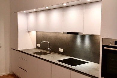 This is an example of a large contemporary single-wall kitchen/diner in Munich with a built-in sink, flat-panel cabinets, white cabinets, concrete worktops, grey splashback, wood splashback, stainless steel appliances, medium hardwood flooring, brown floors and grey worktops.