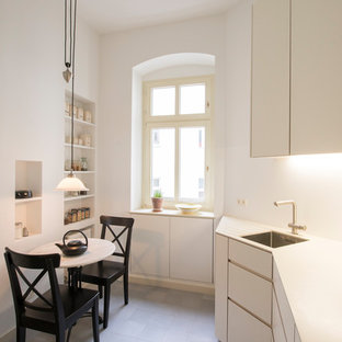 Geschlossene, Einzeilige, Kleine Moderne Küche ohne Insel mit Einbauwaschbecken, flächenbündigen Schrankfronten, weißen Schränken, Küchenrückwand in Weiß, grauem Boden und weißer Arbeitsplatte in Berlin