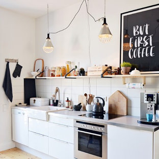 Idées déco pour une petit cuisine américaine linéaire scandinave avec un évier de ferme, un placard à porte plane, des portes de placard blanches, un électroménager en acier inoxydable, un sol en bois clair, aucun îlot, un plan de travail en inox, une crédence blanche et une crédence en carreau de céramique.