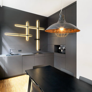 Kleine Industrial Küche mit Einbauwaschbecken, flächenbündigen Schrankfronten, schwarzen Schränken, Küchenrückwand in Schwarz und braunem Holzboden in Nürnberg