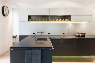 Offene Moderne Küche mit Unterbauwaschbecken, flächenbündigen Schrankfronten, grauen Schränken, Küchenrückwand in Weiß und Halbinsel in Köln