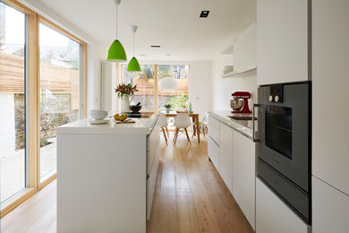 Offene, Einzeilige, Mittelgroße Moderne Küche mit Einbauwaschbecken, weißen Schränken, Küchenrückwand in Weiß, braunem Holzboden, Kücheninsel, braunem Boden und flächenbündigen Schrankfronten in London