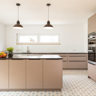 Offene, Große Moderne Küche in L-Form mit Waschbecken, Kassettenfronten, beigen Schränken, Küchenrückwand in Weiß, Glasrückwand, Terrakottaboden, Kücheninsel, buntem Boden, Elektrogeräten mit Frontblende und schwarzer Arbeitsplatte in Frankfurt am Main