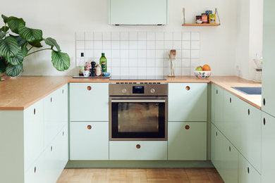 ベルリンにある小さな北欧スタイルのおしゃれなキッチン (フラットパネル扉のキャビネット、緑のキャビネット、木材カウンター、淡色無垢フローリング、白いキッチンパネル、シルバーの調理設備、ドロップインシンク、セラミックタイルのキッチンパネル) の写真