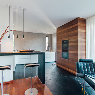 Offene, Mittelgroße Moderne Küche in L-Form mit Unterbauwaschbecken, flächenbündigen Schrankfronten, Mineralwerkstoff-Arbeitsplatte, Küchenrückwand in Grau, schwarzen Elektrogeräten, Schieferboden, schwarzem Boden, weißer Arbeitsplatte, hellbraunen Holzschränken und Halbinsel in Frankfurt am Main