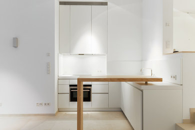 Idéer för att renovera ett litet funkis vit vitt kök, med en undermonterad diskho, släta luckor, vita skåp, laminatbänkskiva, vitt stänkskydd, rostfria vitvaror, klinkergolv i keramik, en halv köksö och beiget golv