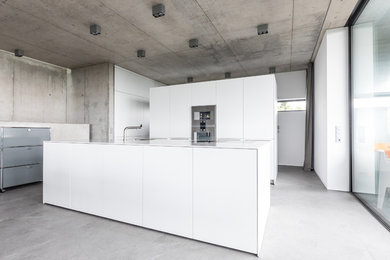 Diseño de cocina minimalista grande abierta con fregadero de un seno, puertas de armario blancas, electrodomésticos de acero inoxidable, una isla, armarios con paneles lisos, suelo de cemento y suelo gris