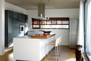 Exempel på ett mellanstort modernt kök med öppen planlösning, med en integrerad diskho, bänkskiva i rostfritt stål, rostfria vitvaror, mellanmörkt trägolv, en köksö, släta luckor och grå skåp