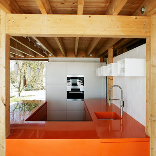Inspiration for a mid-sized contemporary u-shaped open plan kitchen in Munich with an undermount sink, flat-panel cabinets, orange cabinets, solid surface benchtops, black appliances, grey floor and orange benchtop.