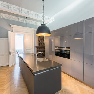 Geschlossene Moderne Küche mit Waschbecken, flächenbündigen Schrankfronten, grauen Schränken, schwarzen Elektrogeräten, hellem Holzboden, Kücheninsel, beigem Boden und schwarzer Arbeitsplatte in Frankfurt am Main