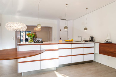 Offene, Große Moderne Küche mit flächenbündigen Schrankfronten, weißen Schränken, Küchenrückwand in Weiß, hellem Holzboden und Halbinsel in Hamburg