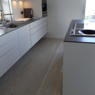 Inspiration for a mid-sized scandinavian galley open plan kitchen in Berlin with an integrated sink, flat-panel cabinets, light wood cabinets, limestone benchtops, white splashback, ceramic splashback, stainless steel appliances, light hardwood floors and with island.