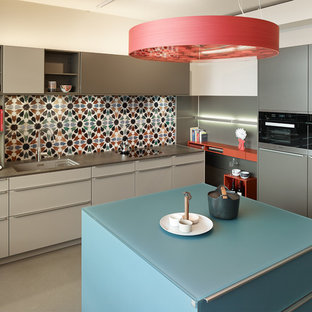 Moderne Küche mit Waschbecken, flächenbündigen Schrankfronten, grauen Schränken, bunter Rückwand, schwarzen Elektrogeräten, Kücheninsel, grauem Boden und grauer Arbeitsplatte in Frankfurt am Main