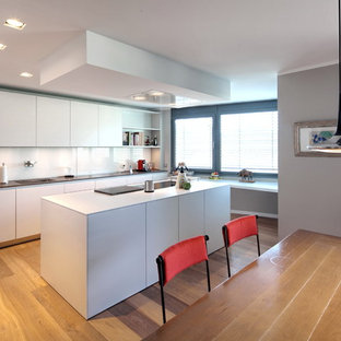 Offene, Einzeilige, Geräumige Moderne Küche mit Waschbecken, flächenbündigen Schrankfronten, weißen Schränken, Küchenrückwand in Weiß, Glasrückwand, Kücheninsel, braunem Holzboden und braunem Boden in Bonn