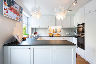 Kleine Moderne Küche ohne Insel in U-Form mit weißen Schränken, Granit-Arbeitsplatte, Küchenrückwand in Grau, schwarzen Elektrogeräten, braunem Holzboden, braunem Boden und schwarzer Arbeitsplatte in München