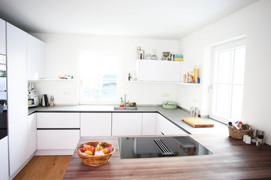 Foto di una grande cucina minimal con lavello integrato, ante lisce, ante bianche, top in acciaio inossidabile, elettrodomestici neri, parquet chiaro e penisola