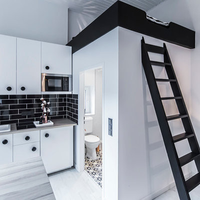 Small trendy single-wall light wood floor eat-in kitchen photo in Dusseldorf with a farmhouse sink, flat-panel cabinets, white cabinets, black backsplash, subway tile backsplash, stainless steel appliances, wood countertops and a peninsula