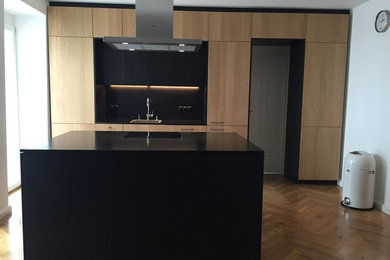 Offene, Zweizeilige, Mittelgroße Moderne Küche mit flächenbündigen Schrankfronten, hellbraunen Holzschränken, Granit-Arbeitsplatte, Küchenrückwand in Schwarz und Kücheninsel in München