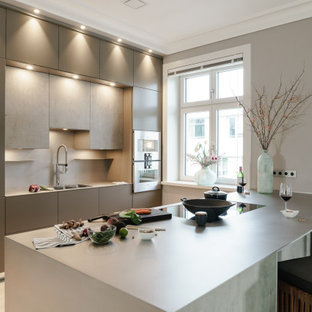 Große Moderne Wohnküche mit flächenbündigen Schrankfronten, Küchengeräten aus Edelstahl, grauer Arbeitsplatte, braunem Holzboden und Halbinsel in Hamburg
