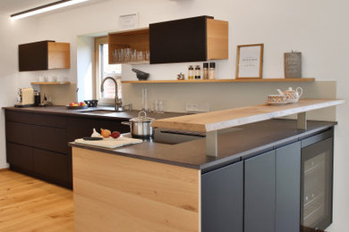 Moderne Küche in L-Form mit Unterbauwaschbecken, flächenbündigen Schrankfronten, schwarzen Schränken, braunem Holzboden, Halbinsel, braunem Boden und grauer Arbeitsplatte in München