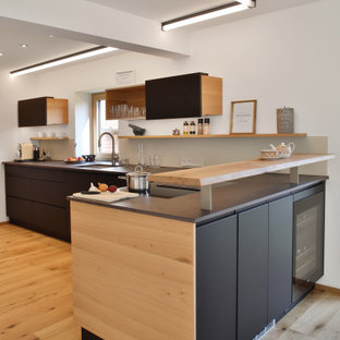 Moderne Küche in L-Form mit Unterbauwaschbecken, flächenbündigen Schrankfronten, schwarzen Schränken, braunem Holzboden, Halbinsel, braunem Boden und grauer Arbeitsplatte in München