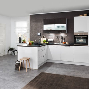 Mid-sized contemporary l-shaped open plan kitchen in Hanover with flat-panel cabinets, white cabinets, brown splashback, black appliances, concrete floors, a peninsula, grey floor, brown benchtop, granite benchtops and slate splashback.