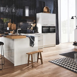 Einzeilige, Kleine Moderne Wohnküche mit Schrankfronten im Shaker-Stil, weißen Schränken, Küchenrückwand in Schwarz, Rückwand aus Metrofliesen, schwarzen Elektrogeräten, braunem Holzboden, Halbinsel, braunem Boden, weißer Arbeitsplatte und Glas-Arbeitsplatte in Hannover