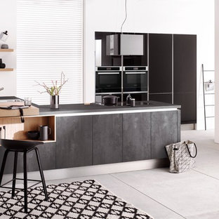 Offene, Mittelgroße Moderne Küche in L-Form mit Einbauwaschbecken, flächenbündigen Schrankfronten, grauen Schränken, schwarzen Elektrogeräten, Betonboden, Halbinsel, grauem Boden, grauer Arbeitsplatte und Granit-Arbeitsplatte in Hannover