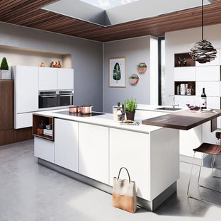 Offene, Große Moderne Küche in L-Form mit Einbauwaschbecken, flächenbündigen Schrankfronten, schwarzen Elektrogeräten, Betonboden, zwei Kücheninseln, grauem Boden, weißer Arbeitsplatte, weißen Schränken und Quarzit-Arbeitsplatte in Hannover