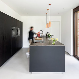 Zweizeilige Moderne Küche mit flächenbündigen Schrankfronten, schwarzen Schränken, schwarzen Elektrogeräten, Betonboden, Kücheninsel, grauem Boden und grauer Arbeitsplatte in Sonstige