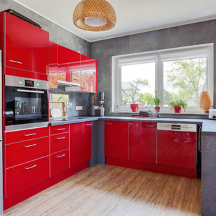Offene, Mittelgroße Moderne Küche ohne Insel in U-Form mit Einbauwaschbecken, flächenbündigen Schrankfronten, roten Schränken, Glasrückwand, Küchengeräten aus Edelstahl, Vinylboden, braunem Boden und grauer Arbeitsplatte in Berlin