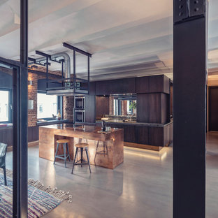 Offene, Zweizeilige, Große Industrial Küche mit flächenbündigen Schrankfronten, braunen Schränken, Rückwand aus Spiegelfliesen, Küchengeräten aus Edelstahl, Betonboden, Kücheninsel, grauem Boden und brauner Arbeitsplatte in Nürnberg