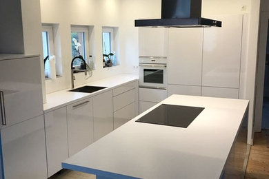 This is an example of a medium sized contemporary galley open plan kitchen in Hanover with a single-bowl sink, flat-panel cabinets, white cabinets, white splashback, white appliances, an island, grey floors, ceramic flooring, composite countertops and glass sheet splashback.