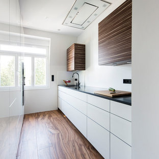 Zweizeilige, Geschlossene, Kleine Moderne Küche ohne Insel mit flächenbündigen Schrankfronten, weißen Schränken, Küchenrückwand in Weiß, dunklem Holzboden, braunem Boden, schwarzer Arbeitsplatte und integriertem Waschbecken in Frankfurt am Main