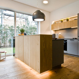 Zweizeilige Moderne Wohnküche mit flächenbündigen Schrankfronten, hellen Holzschränken, Küchenrückwand in Grau, schwarzen Elektrogeräten, braunem Holzboden, Halbinsel, braunem Boden und schwarzer Arbeitsplatte in Nürnberg
